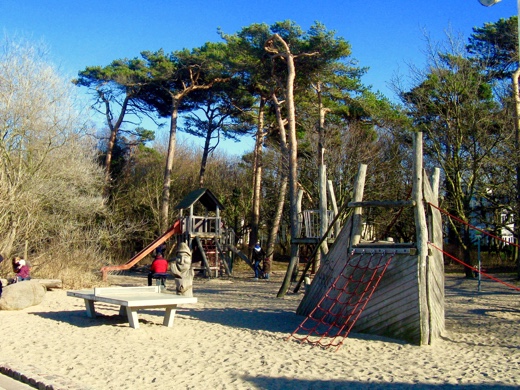 Der Spielplatz beim Haus ist groß mit Sand angelegt und hat mehrere Holzbauten, die zum Klettern einladen sowie Sitzgelegenheiten.